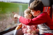 Junge mit kleinem Mädchen fahren Zug und schauen raus, erzeigt etwas in der Landschaft.