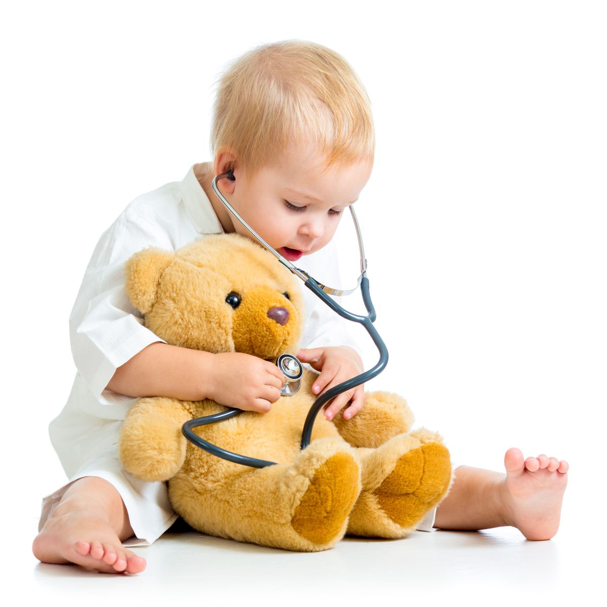 Ein Baby sitzt auf dem Boden untersucht mit Stethoskop seinen Teddy.