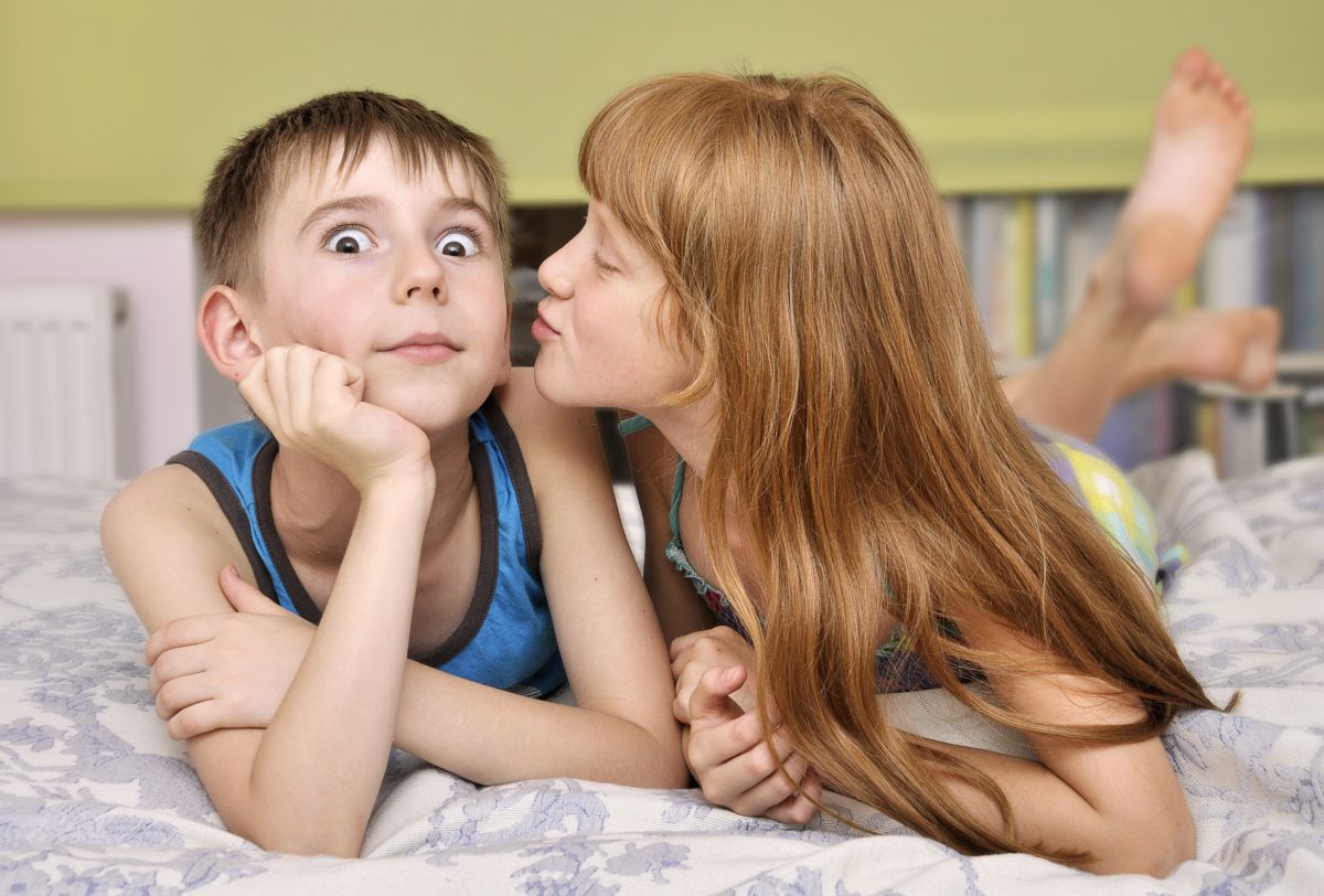 Mädchen und Junge liegen auf dem Bett. küsst Jungen auf die Wange.