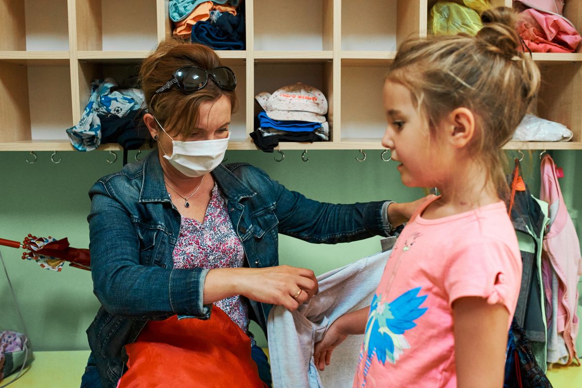 Frau zieht in der Umkleide des Kindergartens ein Mädchen an.