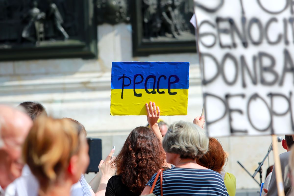 Demonstration mit Menschen, die Plakate hochhalten, darunter eine Ukraine-Flagge mit der Aufschrift Peace.