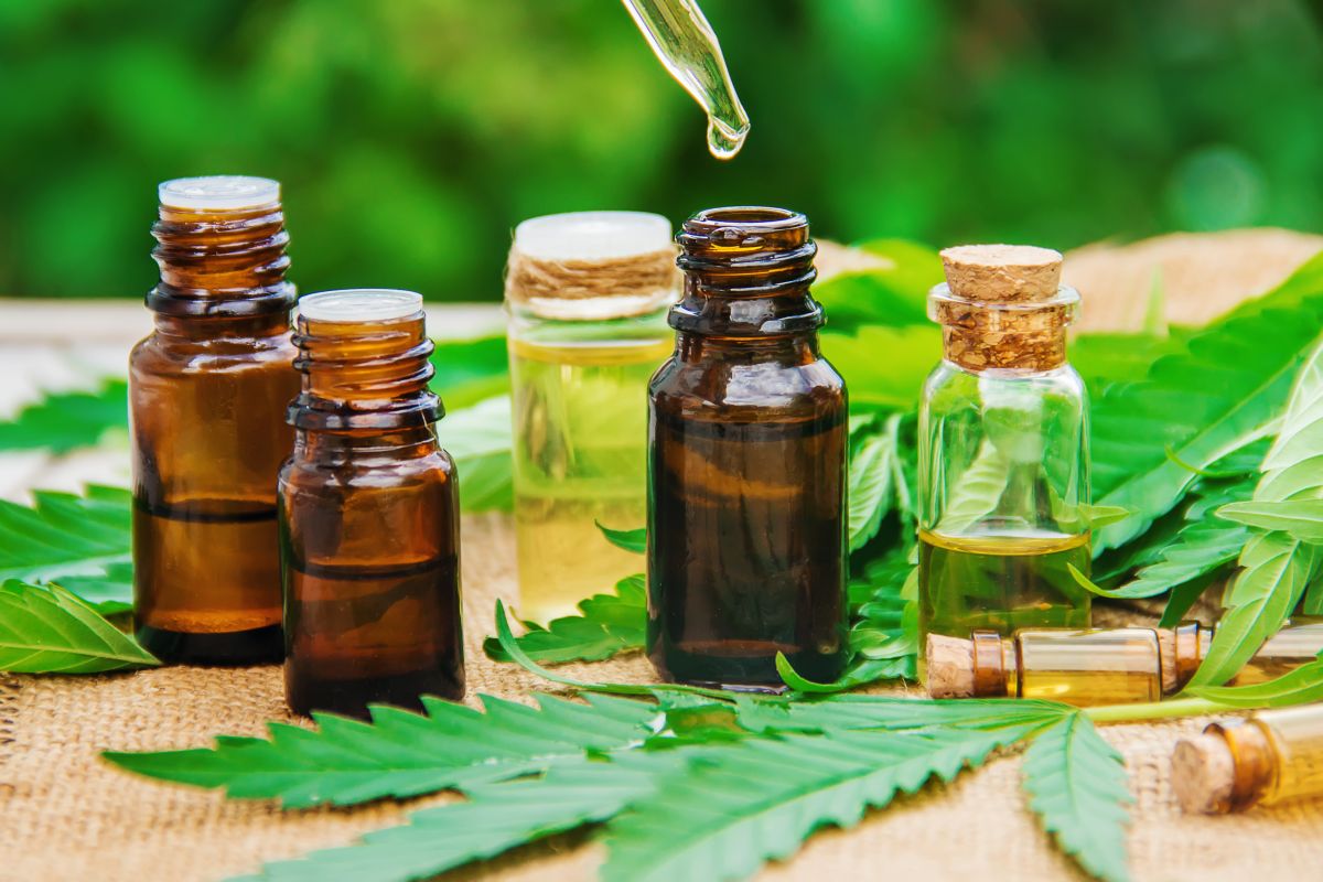 Auf einem Cannabis-Blatt stehen kleine dunkle Fläschchen, in denen sich Öl befindet. Auf einem Cannabis-Blatt stehen kleine dunkle Fläschchen, in denen sich Öl befindet.