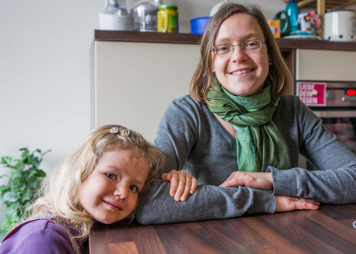 Mädchen mit Mutter am Tisch lächeln in die Kamera.