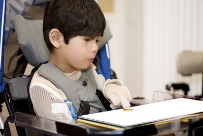 Junge im Rollstuhl lässt sich von Elektronik beim Tippen auf der Tastatur helfen. 