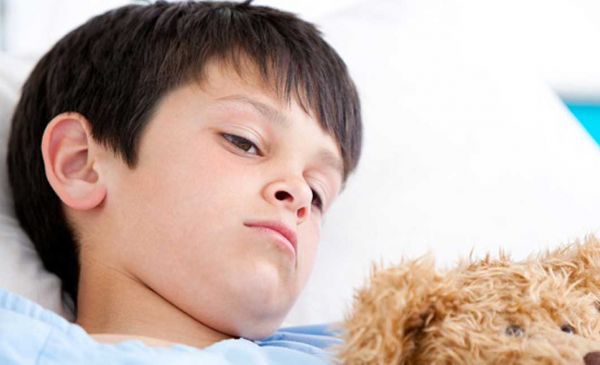 Krankes Kind mit Teddy im Bett.