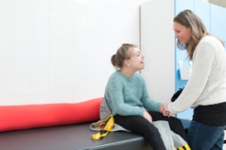 Frau mit behindertem Mädchen., das auf einer Behandlungsliege sitzt.