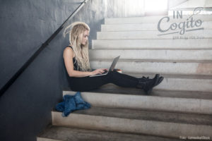 Junges Mädchen sitzt mit ausgestreckten Beinen und ihrem Laptop auf einer Treppe